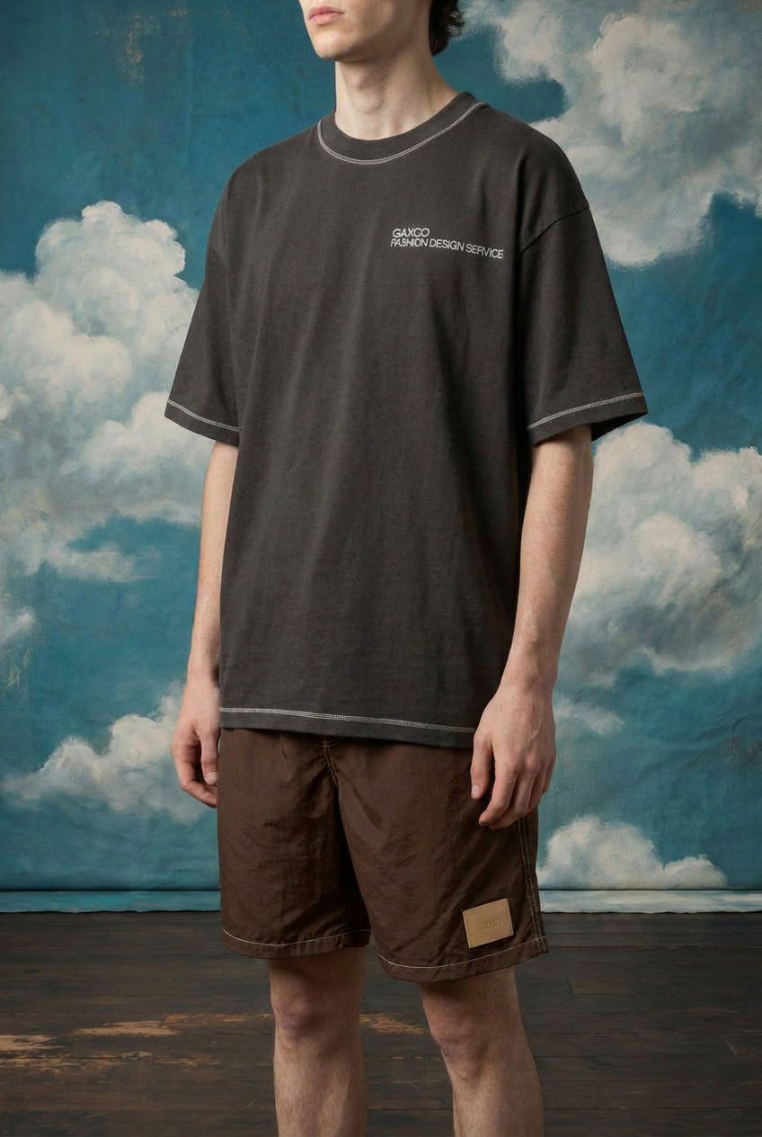 Model wearing Creative Workers oversized tee with brown shorts against a cloud backdrop.