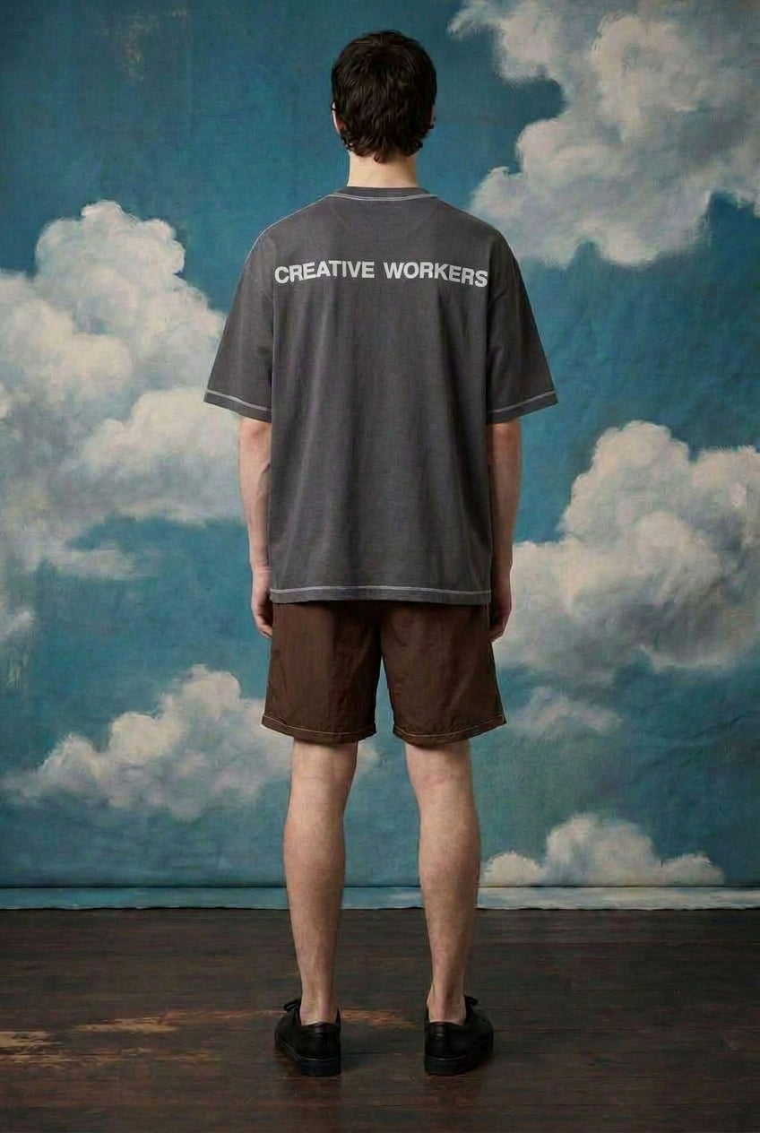 Male model wearing Creative Workers oversized tee with clouds backdrop, showcasing comfort and style.